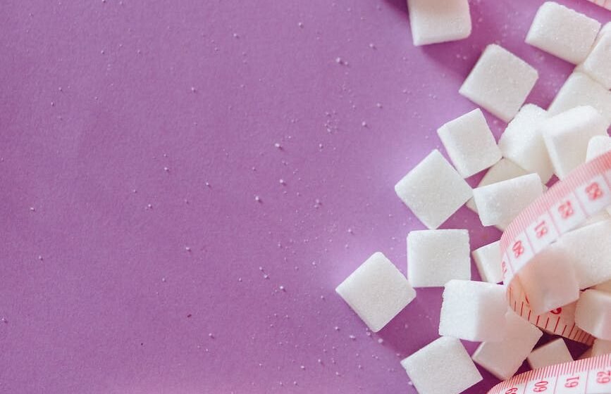 sugar cubes beside tape measure near dices with letter on a pink surface