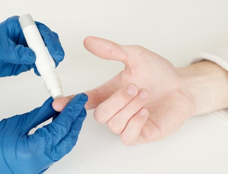 person in blue gloves using a lancet pen on a diabetic person